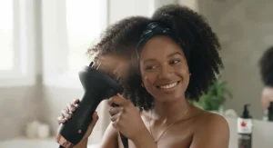A smiling Canadian woman with textured 3C hair using a specialized hair dryer with a diffuser.